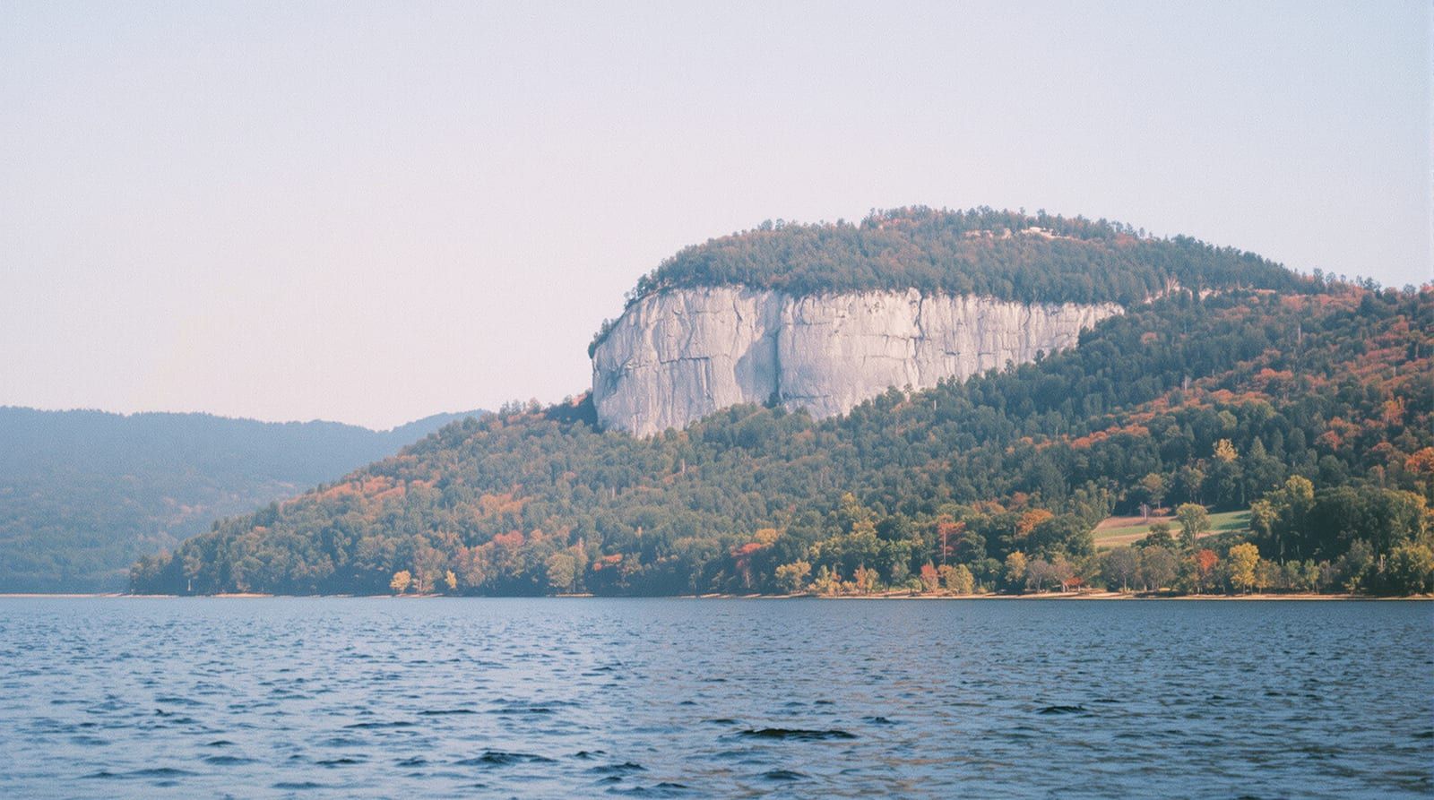A granite cliff face on a forested ridge above a calm reservoir in the foothills