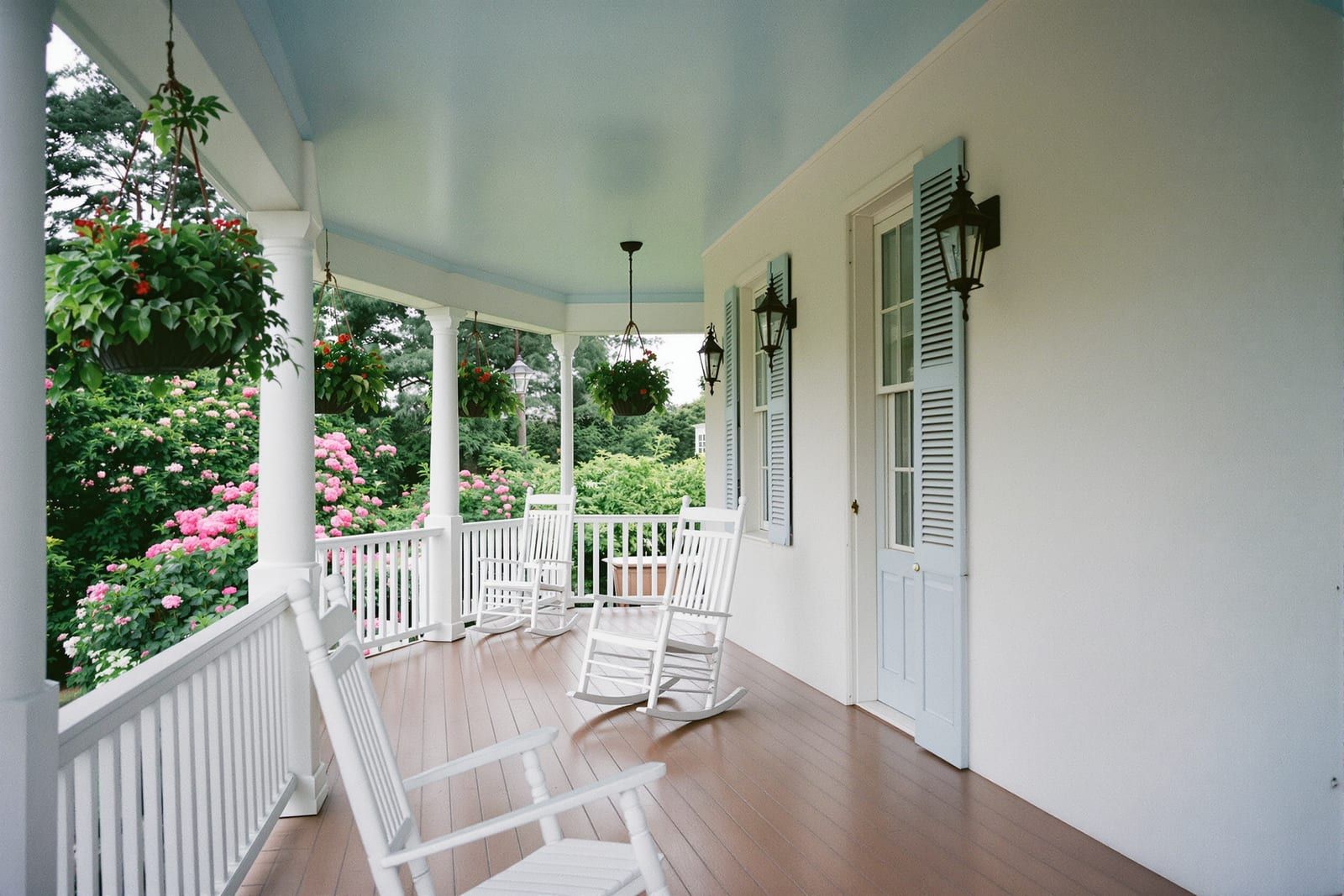 A white front porch with a pale haint-blue ceiling, rocking chairs and hanging ferns
