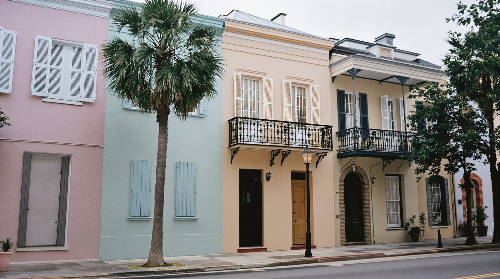 Pastel townhouses with shutters and iron balconies beside a palmetto on an old harbor-city street