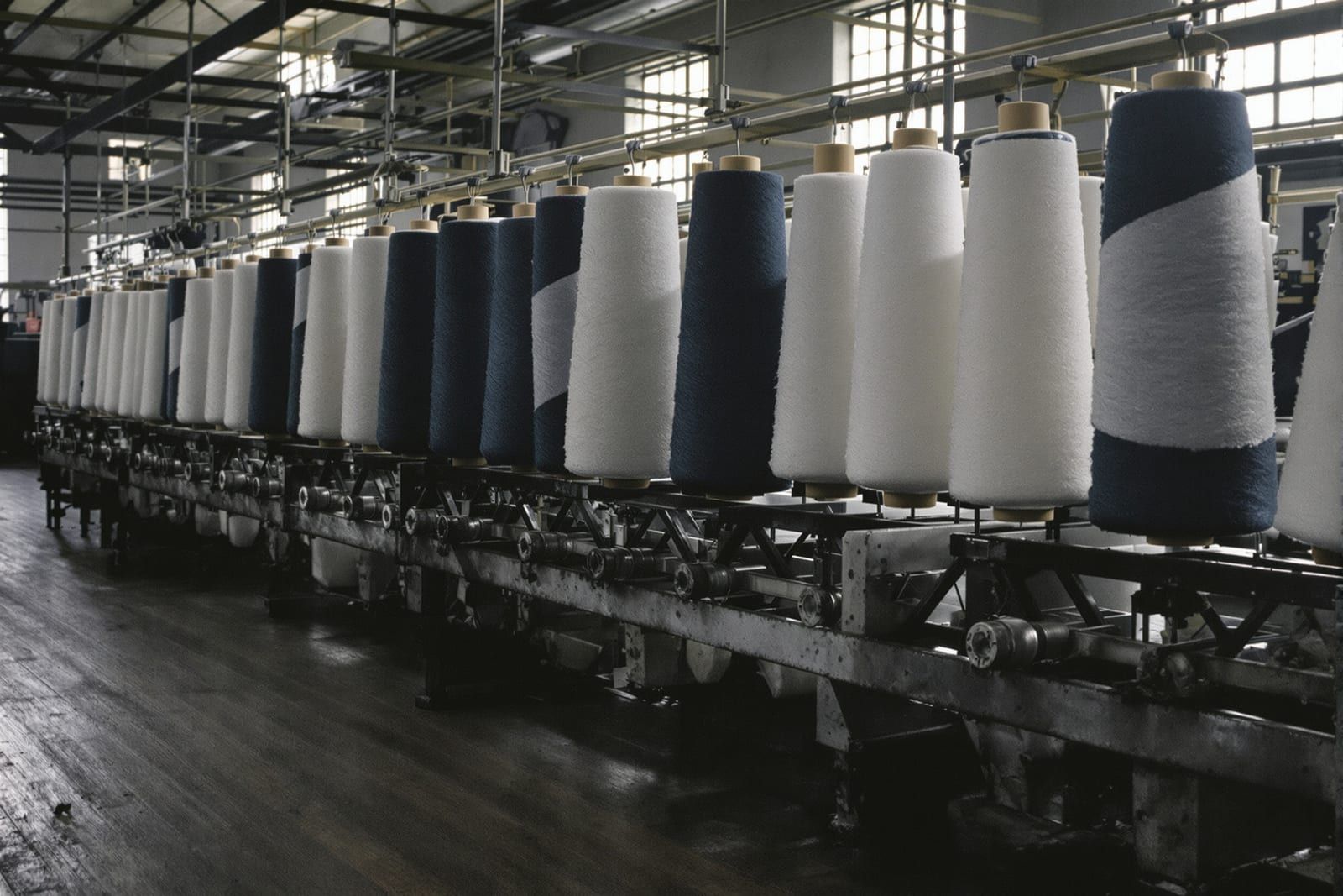 Rows of white and indigo yarn cones on a rack in an old mill